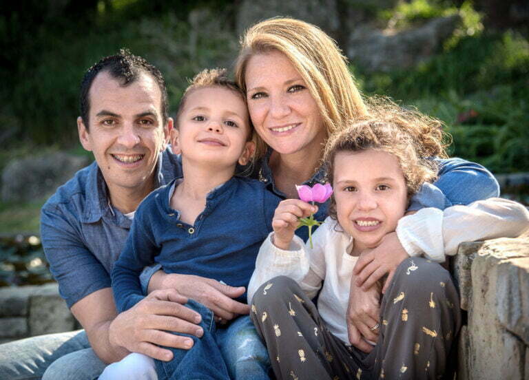 foto de familia en los jardines de mosteen cinto Verdaguer de barcelona. La familia esta mirando a cámara y la niña lleva una flor rosa en la mano